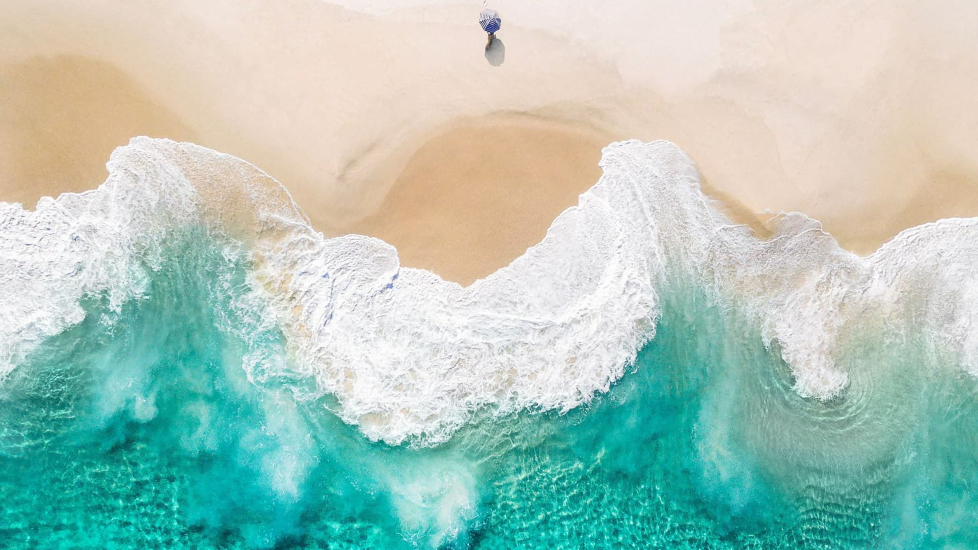 Aerial view of turquoise waves on a sandy beach