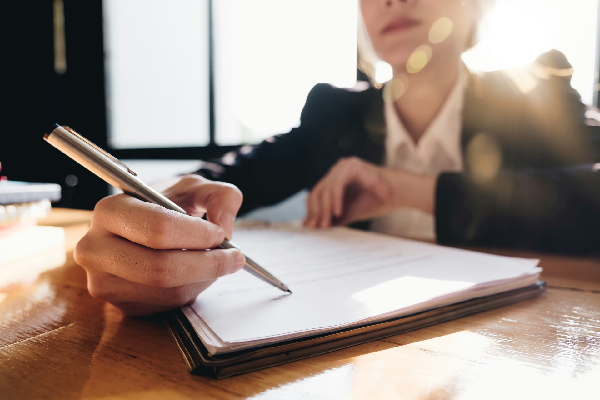 Close-up of a hand signing hotel investment documents at a wooden desk